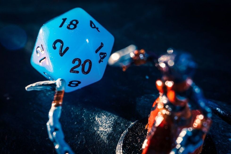 Close-up of a blue twenty sided dice and a role playing mini on a dark surface.