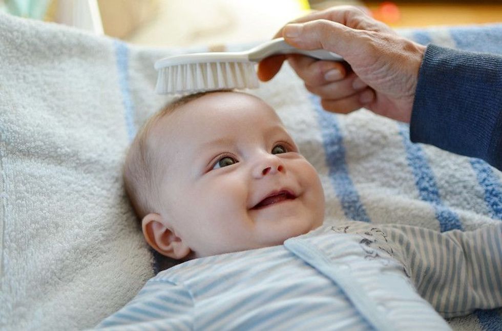 Close up of a smiling baby with his hair being brushed