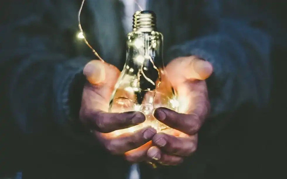 Close up of hands holding a lightbulb with lights inside shining.