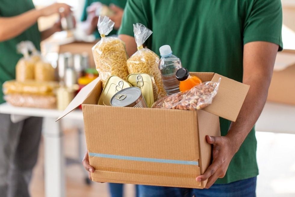close up of male volunteer's hands holding box with food over group of people at distribution
