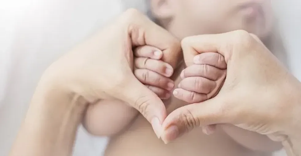  Close up of mother holding hands of her newborn baby in heart shape