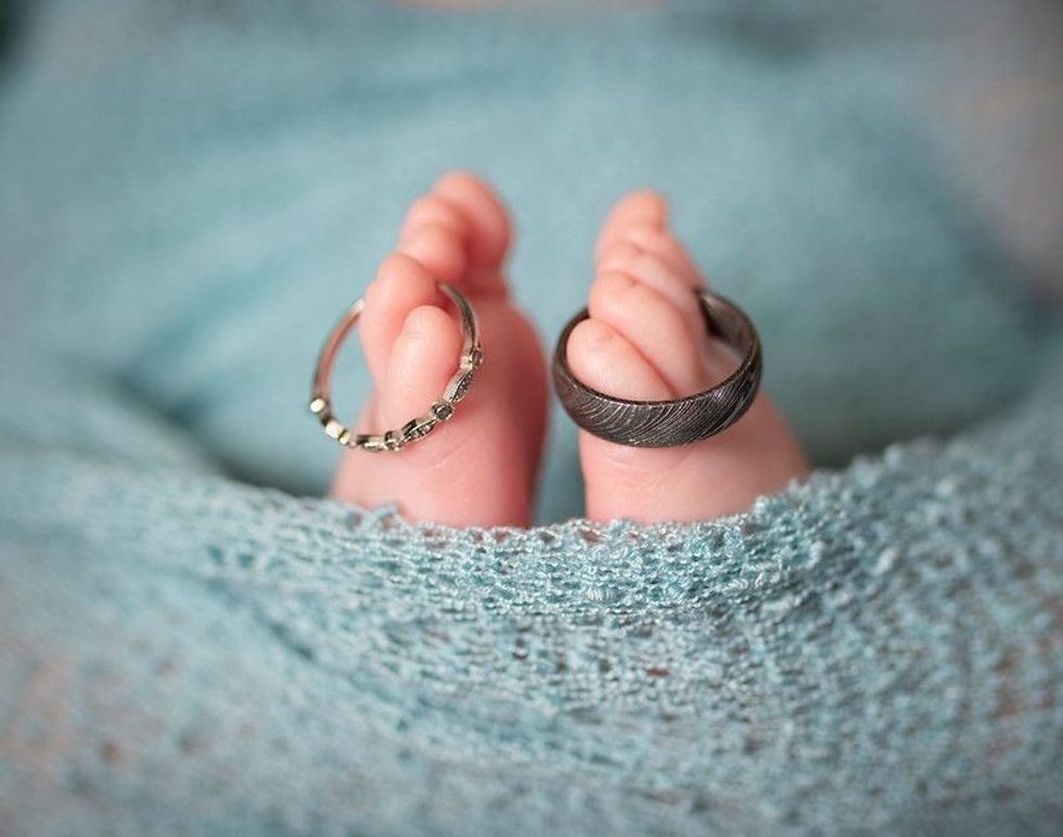 Close up of newborn feet with tiny toes wearing parent silver wedding rings