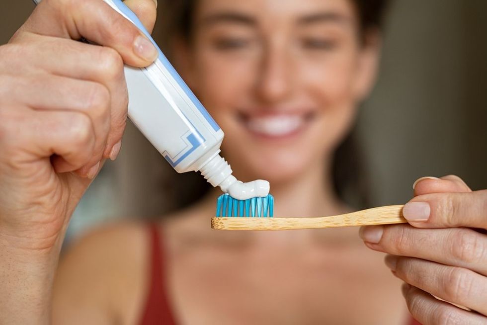 Close up of woman with tooth brush applying paste in bathroom.