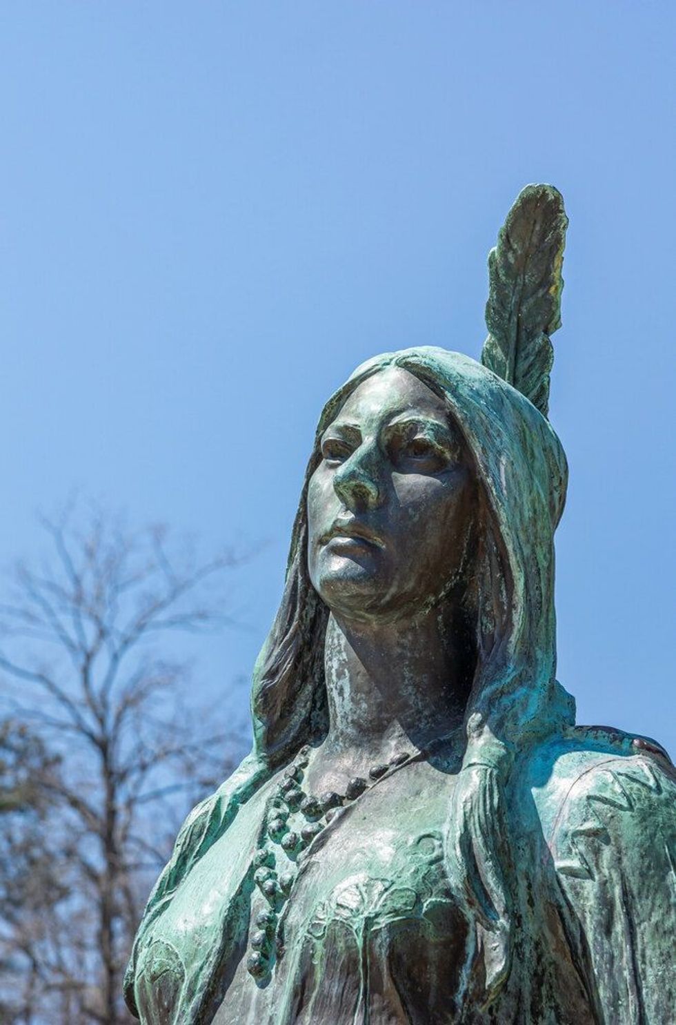Closeup of Pocahontas face on bronze statue against blue sky.