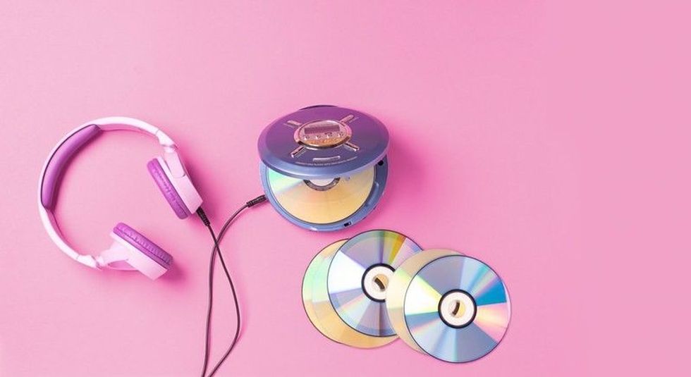 Compact portable CD player disks, CDs & purple headphones on a pink background.