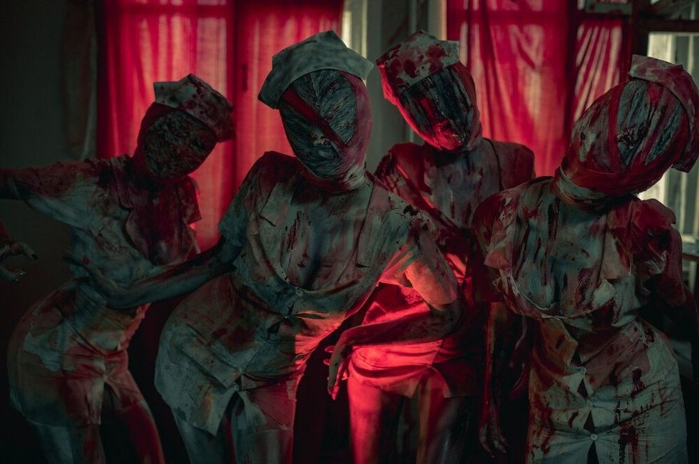 Cosplayers in the image of Dark Nurses from the horror movie "Silent Hill" stand in dark room