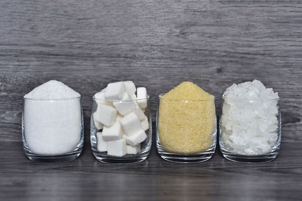 Cube sugar, raw sugar , crystalline sugar and granulation sugar in clear glasses with grey wooden background