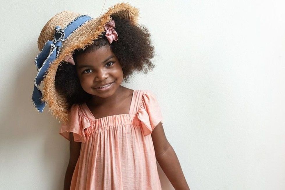Cute afro little girl with straw hat wearing old rose color dress.