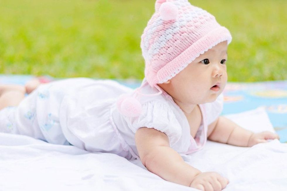 Cute Asian baby lie prone on ground at park.