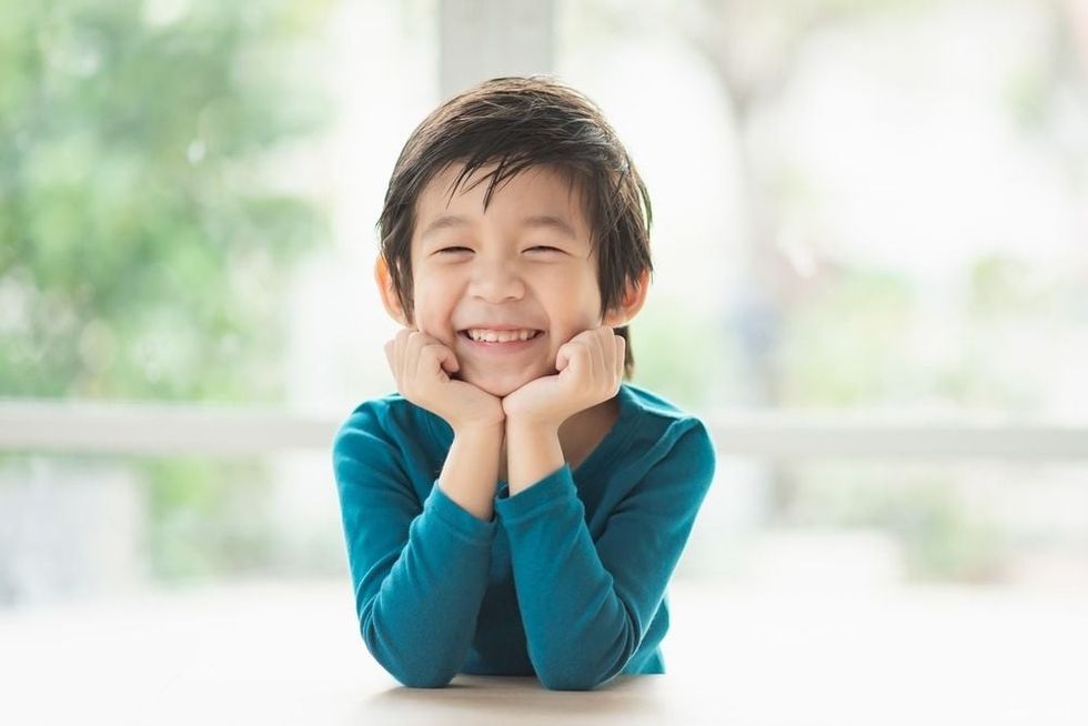 Cute Asian child resting chins on hands on wood table.