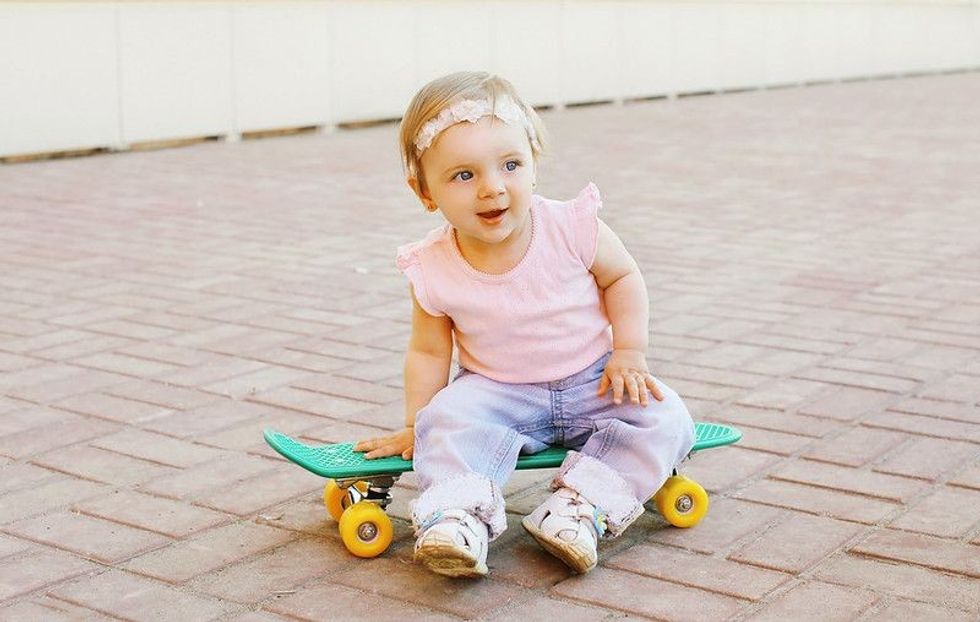 Cute baby girl sitting on a teal skateboard