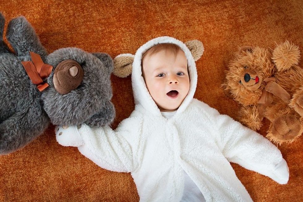 Cute baby wearing bear costume lying on bed with teddy bears.
