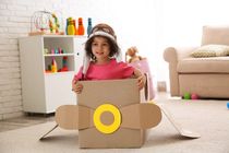 Cute girl dressed as aviator sitting in cardboard airplane