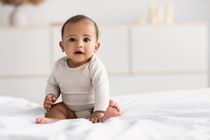 Cute little African American infant sitting on bed