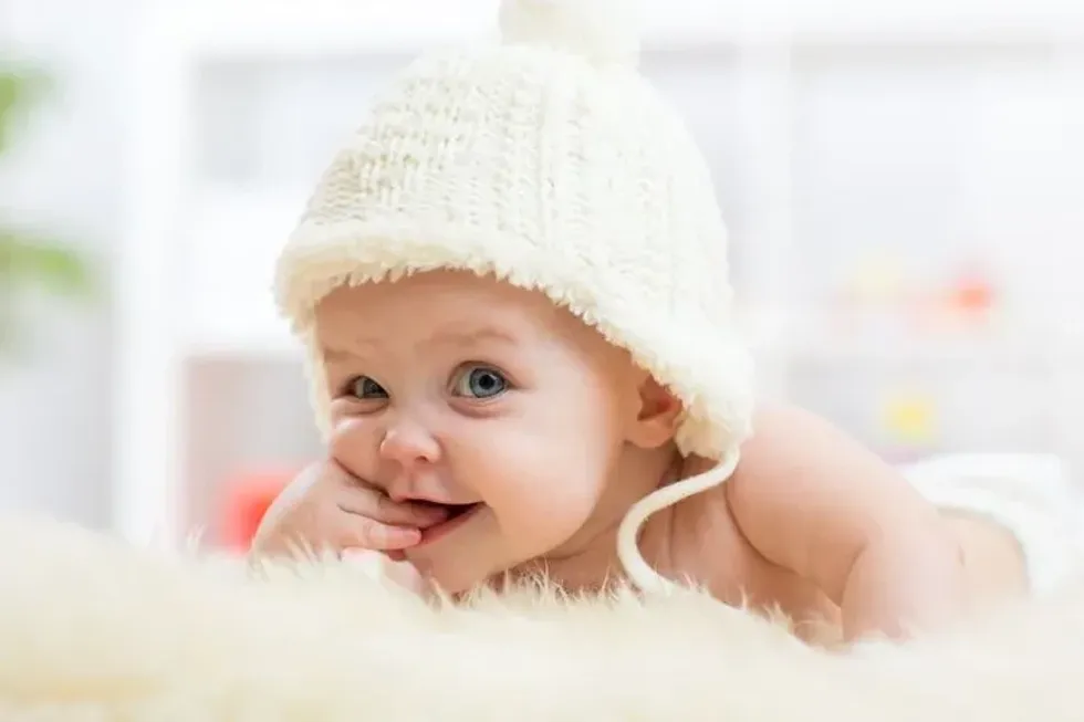 Cute little baby girl looking into the camera wearing a white hat.