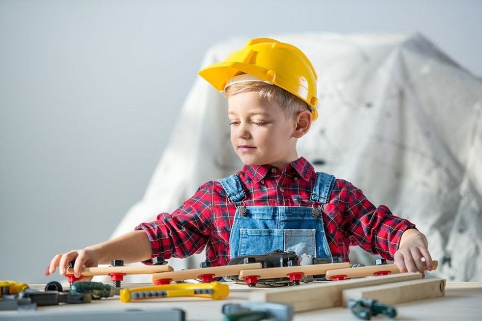 Cute little boy in yellow hard hat playing with toy tools