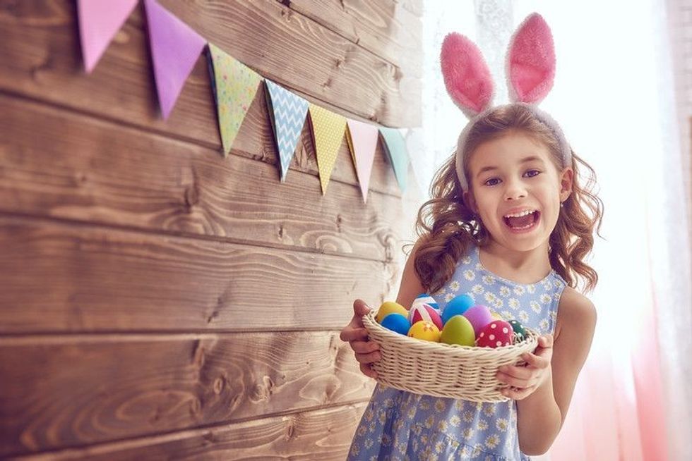 Cute little child wearing bunny ears holding basket with painted eggs on Easter day