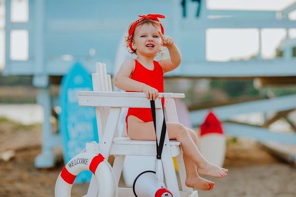 Cute little girl in red bikini and headband sitting on white lifeguard chair