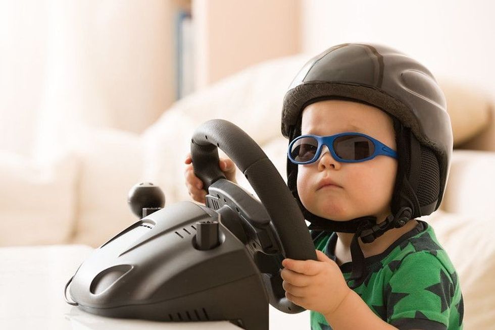 Cute little kid boy in a helmet playing with Computer steering wheel