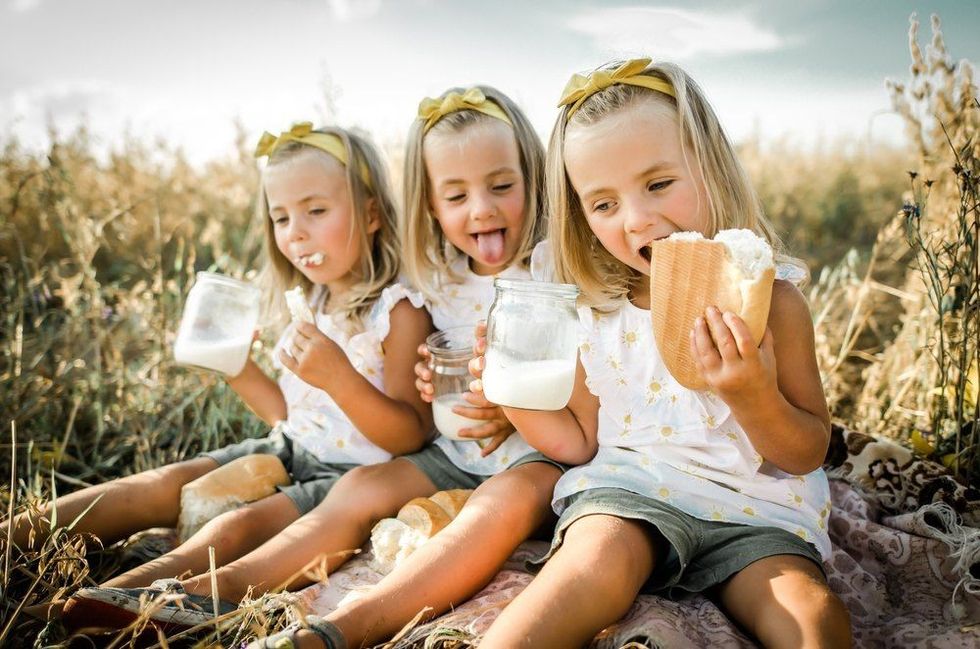 Cute triplet sisters in the field eating bread with milk.