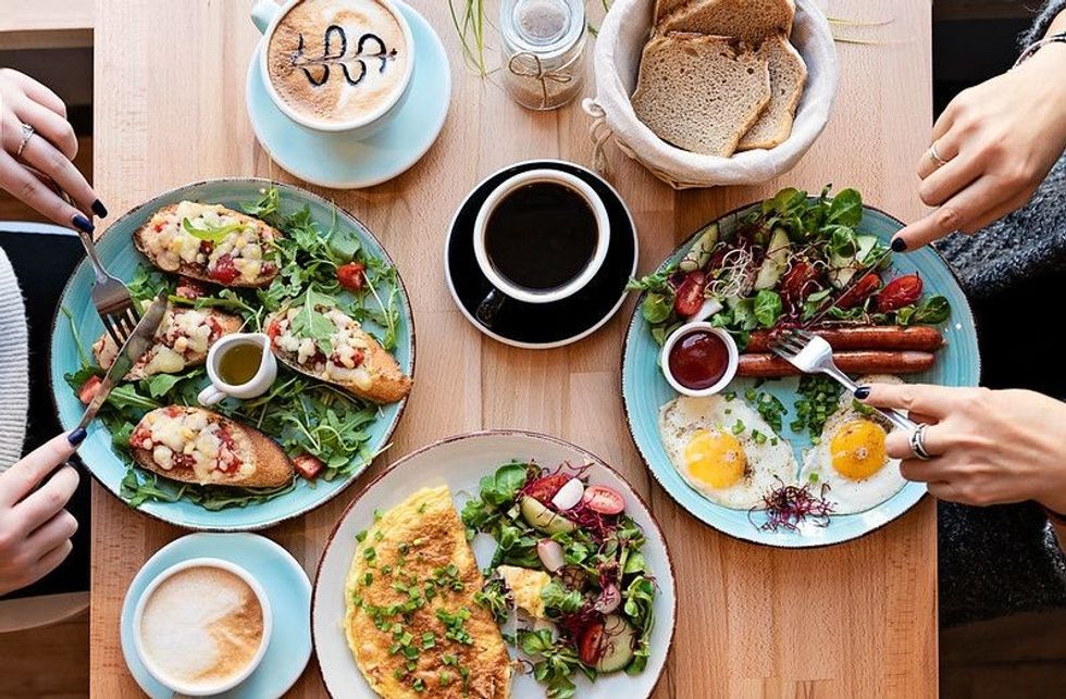 Different colorful meals for breakfast or lunch time on a plate with cutlery on woman's hands
