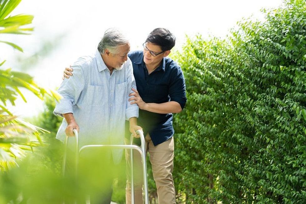 Elderly Asian father and Adult son walking in backyard representing national caregivers day.