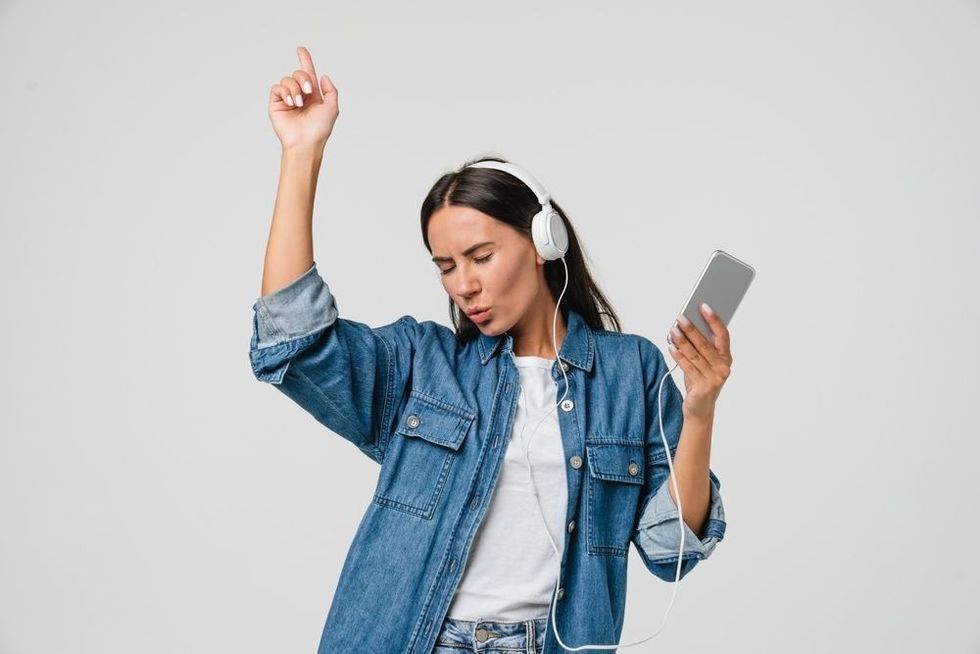 Energetic young woman dancing singing listening to the music podcast with headphones.
