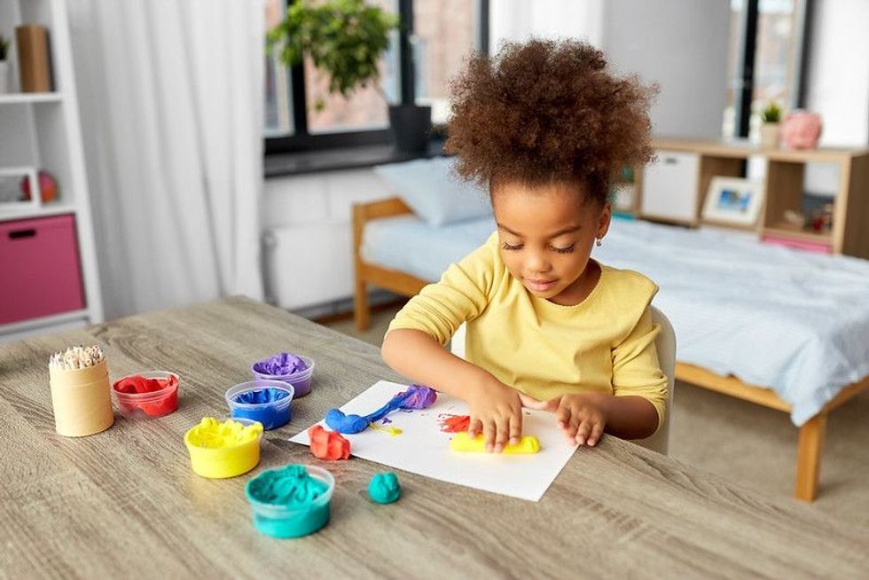 Ethnic baby girl playing with colorful clay dough