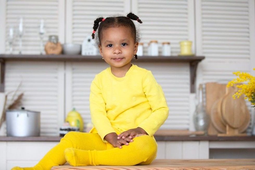 Ethnic baby girl wearing yellow clothes sitting in kitchen