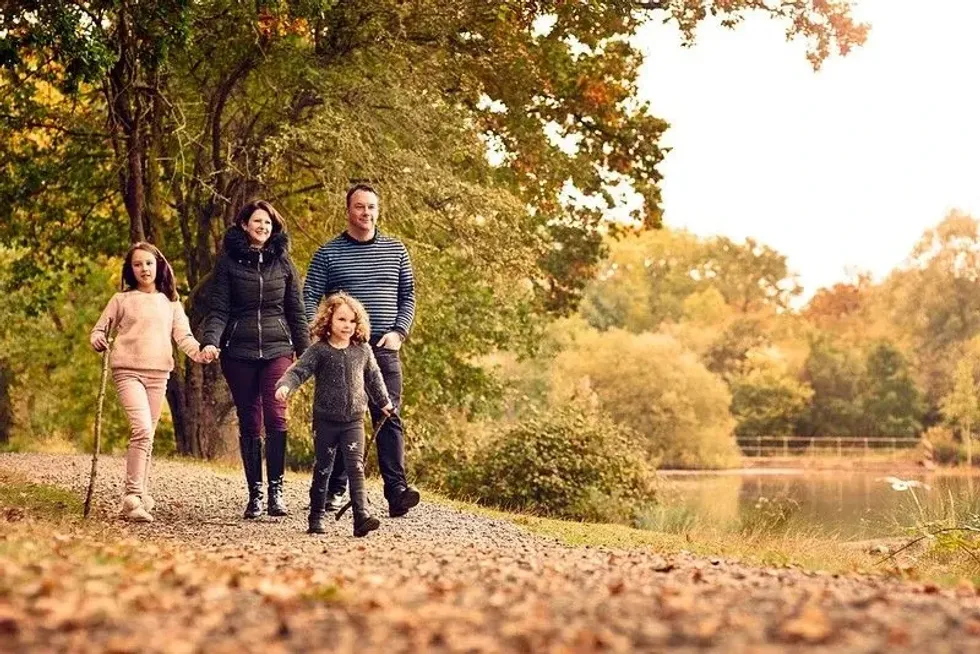 Family walking happily along nature trail with autumnal trees in the background, next to lake.