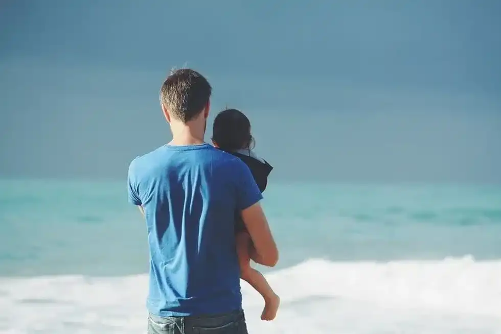 Father and daughter at the beach looking out at the sea.