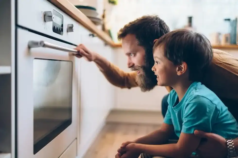 Father and son in the kitchen cooking Roman recipes together, crouching down to peer through the oven window.