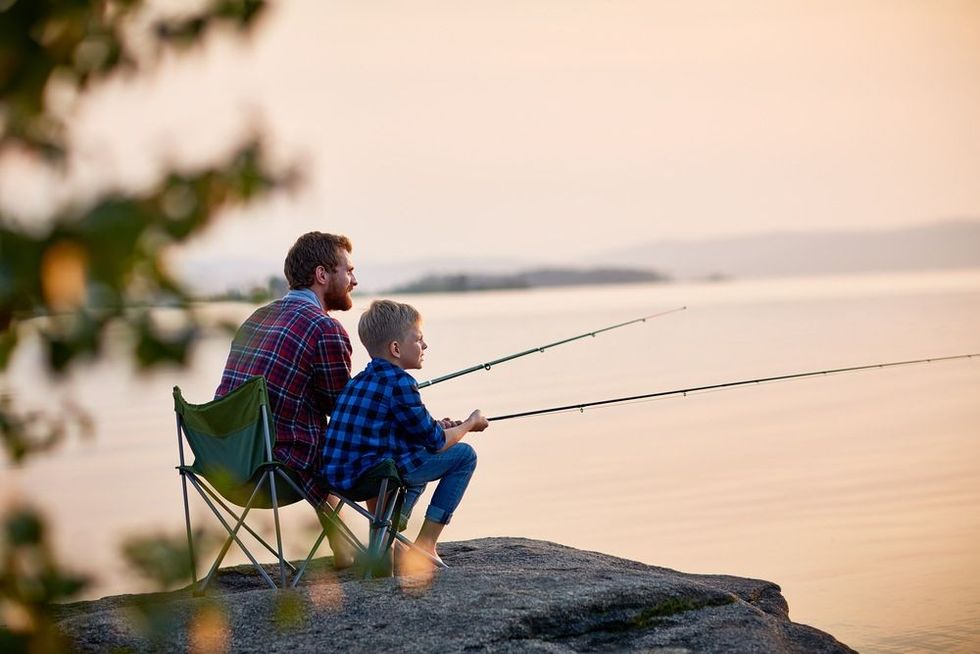 Father and son sitting together on rocks fishing with rods