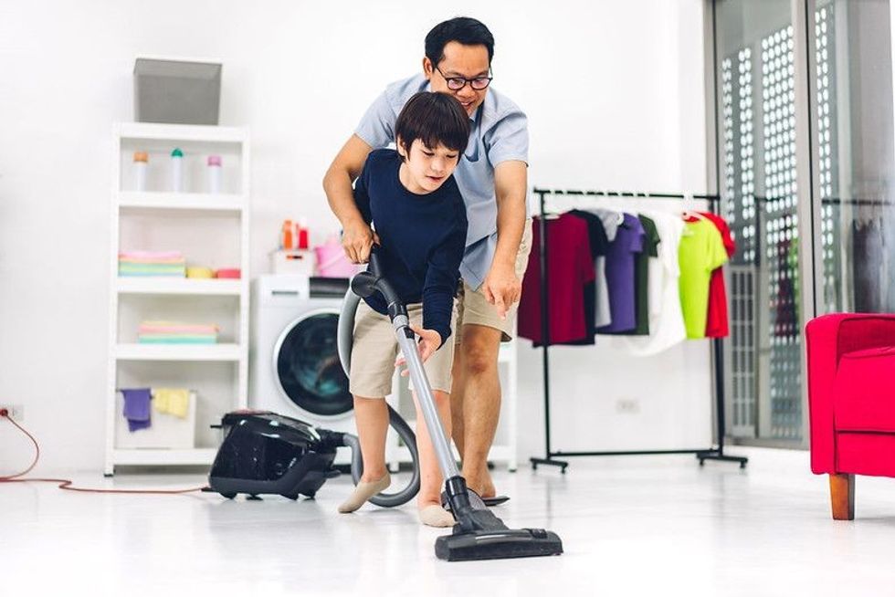 Father teaching his son household chores, cleaning and washing floor and wiping dust with vacuum cleaner.