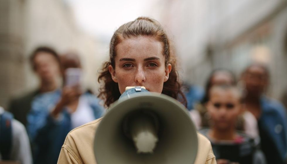 Female activist protesting with megaphone during a strike with group of demonstrator in background.