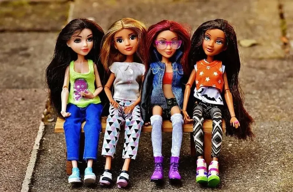 Four Barbie dolls wearing chic outfits sat on a bench together.