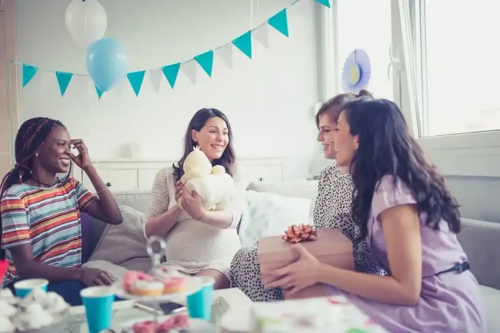Four girlfriends at a baby shower enjoying themselves while opening the gifts.