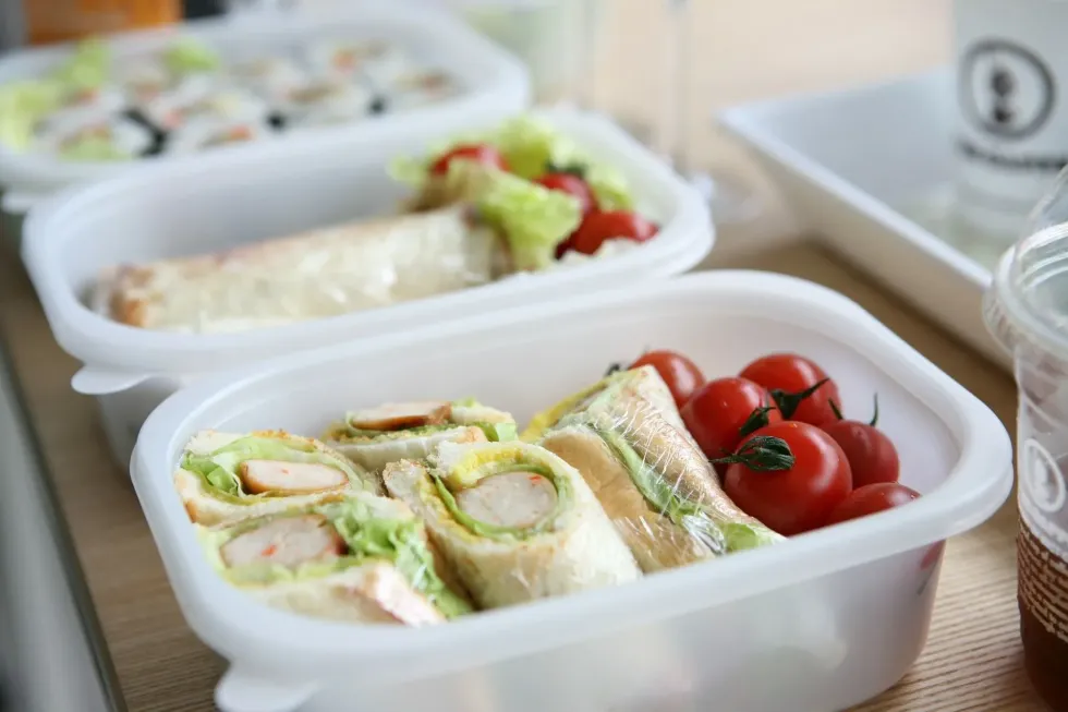  Freshly prepared wrap sandwiches and cherry tomatoes in a takeout container, an ideal quick and healthy lunch option.