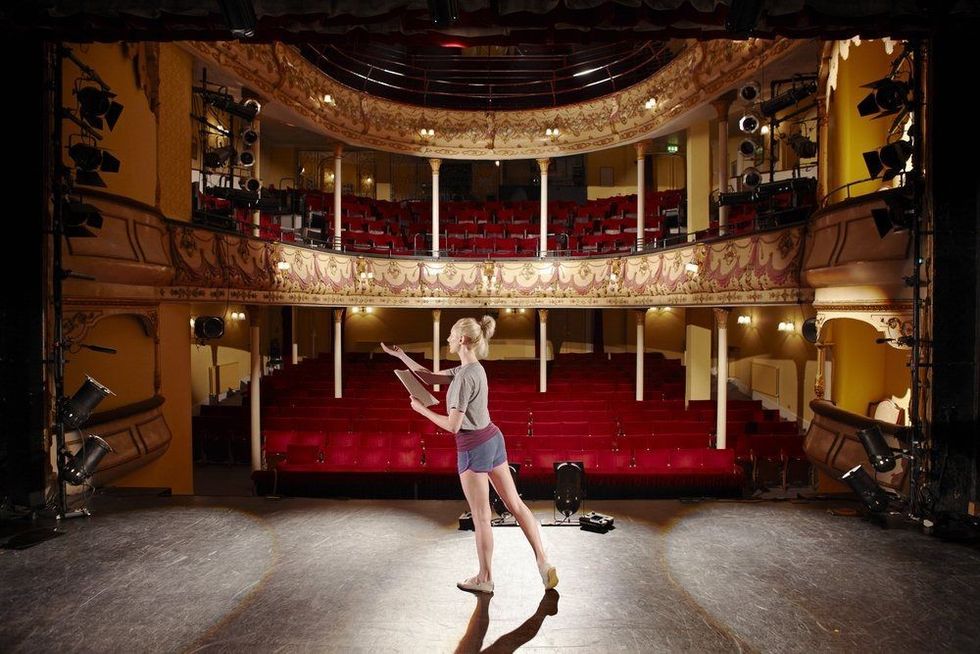 Full length of a young woman with script rehearsing on stage.