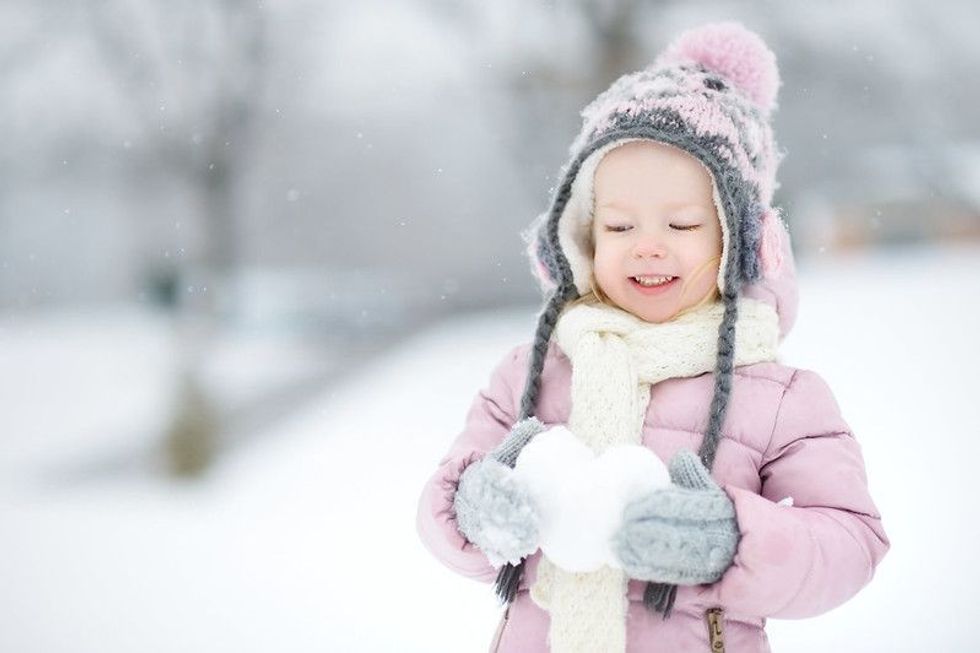 Funny little girl holding snow heart in beautiful winter park during snowfall