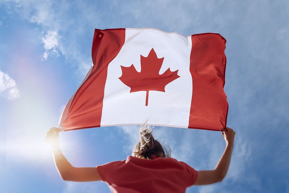 Girl is waving Canadian flag on top of mountain at sky