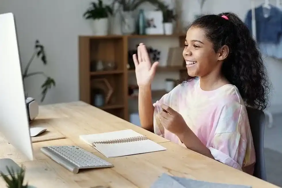 Girl sat at a table in front of a computer looks happy while studying.