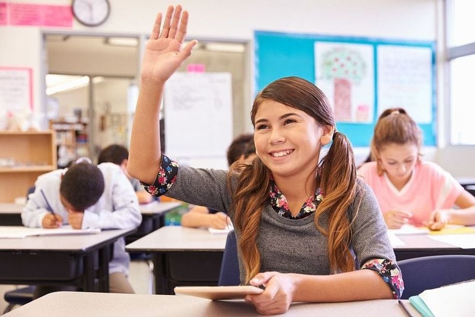 Girl sitting in a classroom and taking initiative to answer a question