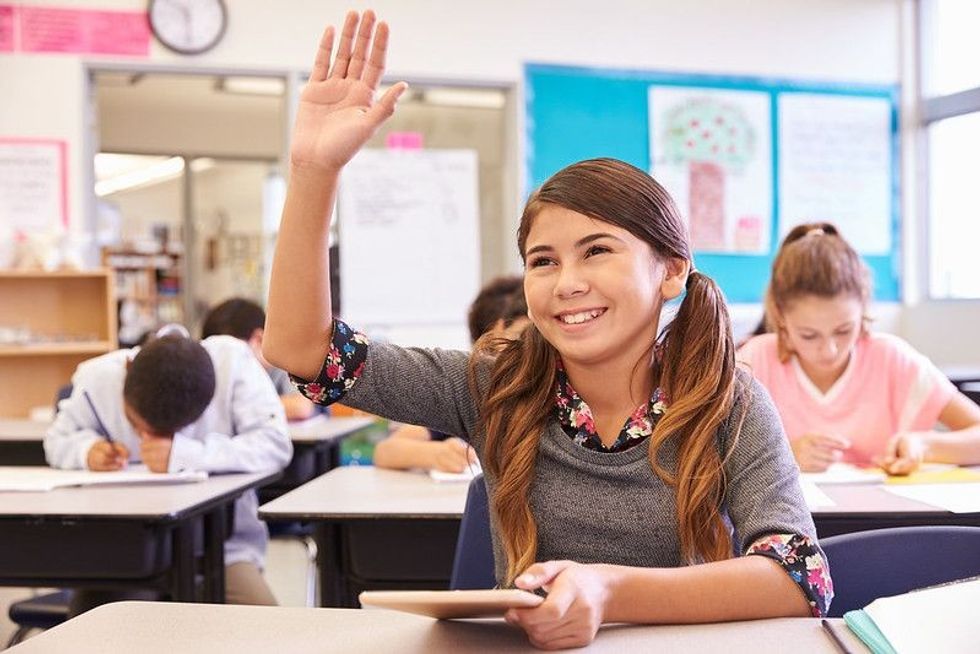 Girl with tablet raising hand in elementary school class