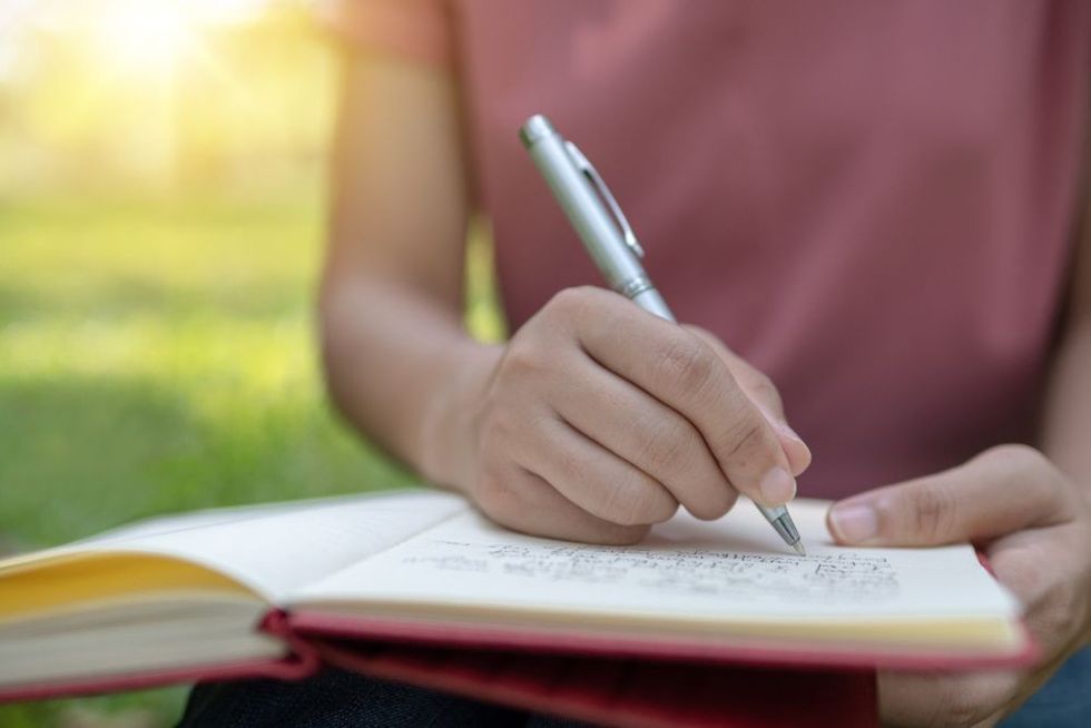 girl writing poetry on notebook in park