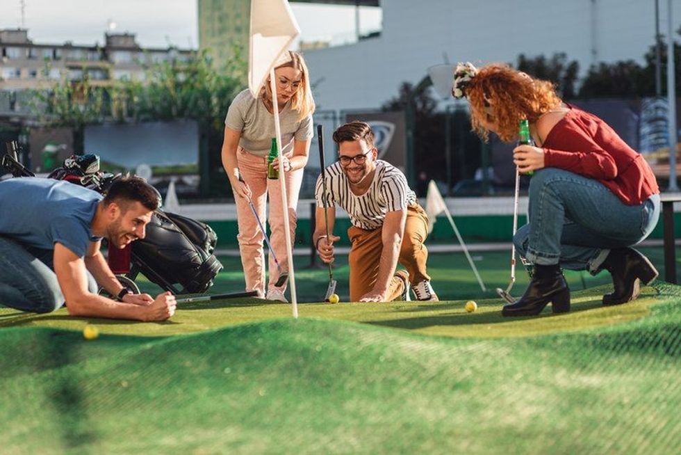 Group of friends enjoying together while playing mini golf in the city.