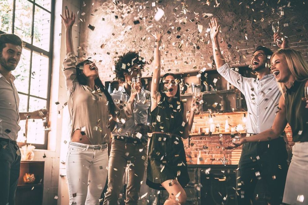 Group of happy young people throwing confetti and jumping while enjoying home party