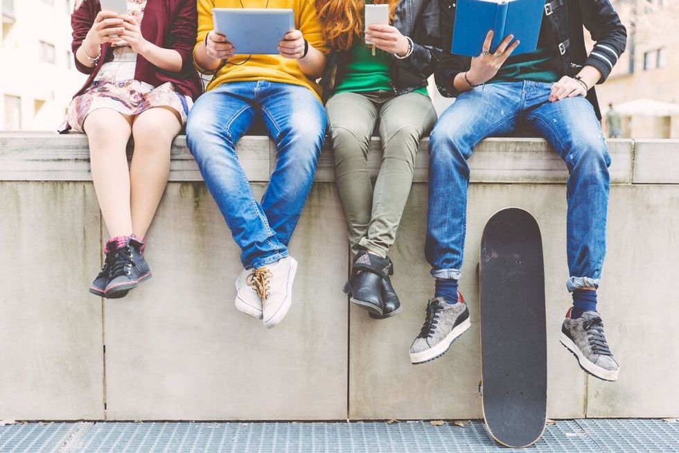 Group of teenagers making different activities sitting in an urban area.