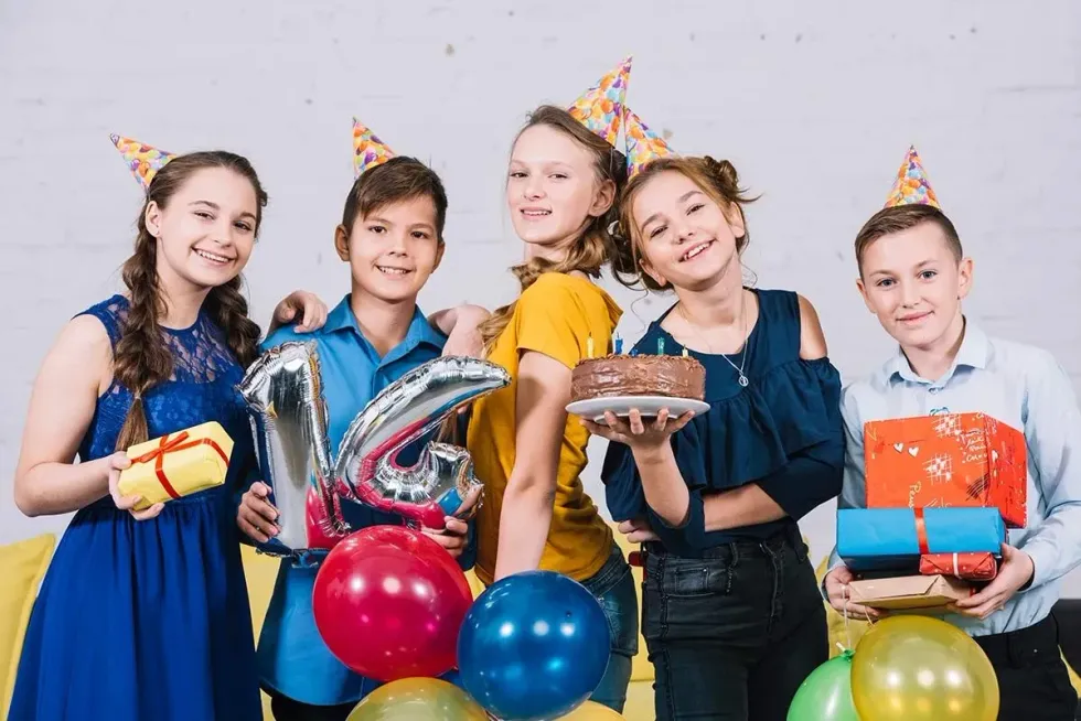 Group of teens wearing party hats and posing smiling at birthday party with a cake.