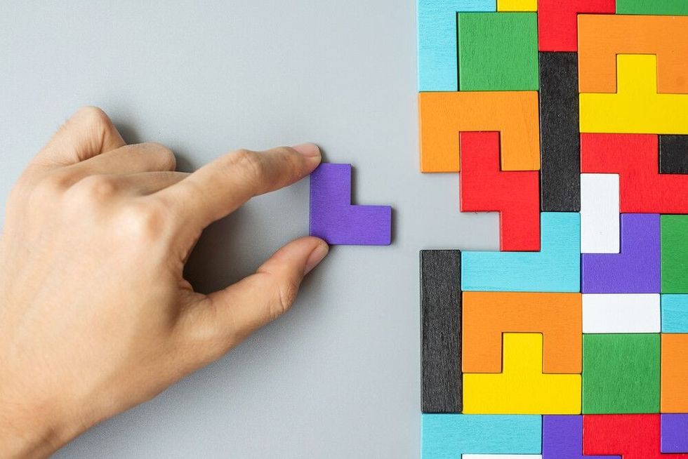 hand connecting geometric shape block with colorful wood puzzle pieces.
